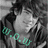 Pixelated grayscale image of a person with dark hair and light clothing, featuring teal-colored text overlay reading "0.0.0" on the left side.