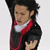 Pixelated static image of a figure skater in mid-performance wearing a black and red costume with white collar, viewed from side angle against light gray background.