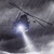 A static pixelated image shows a dark, abstract shape with a bright white light source at its center, set against a gray gradient background with darker edges.