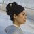 Pixelated profile view of a person with dark hair in a bun, wearing a light blue top against a blurred background.