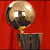 A golden trophy with a reflective spherical top and dark base against a solid red background.
