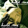 A close-up of a person with dark hair lying down, wearing a light-colored hooded garment, with text overlays reading "hold me" and "need to feel your arms".