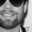 Black-and-white close-up of a person wearing dark sunglasses and a collared shirt, with visible facial hair.