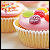 Pixelated static image of a cupcake with pink frosting, berries, and sprinkles on a wooden surface.
