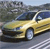 Static image of a yellow sedan on a road with blurred background elements including trees and sky.