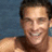 Pixelated close-up of a person with dark hair against a blue background, showing upper torso and smiling expression.