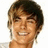 Pixelated image of a smiling person with brown hair and earrings, surrounded by blue text reading "He's so gay after all" in multiple variations.