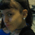 A pixelated close-up of a person's face with dark hair, visible ear, and blue clothing against a blurred background.