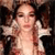 A pixelated image of a person with light skin tone, long brown hair, and closed eyes, wearing a white sleeveless top against a dark background.