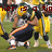 Football players in yellow and dark blue uniforms on a grass field with overlaid red text fragments.