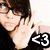 A person with dark hair and glasses makes a hand gesture near their face, with a '<3' symbol in the corner.