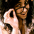 Pixelated image of a person with brown hair holding a white object near their face against dark background.