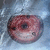 A circular red and brown icon with a central dark eye-like shape, surrounded by a light blue background with white highlights, showing subtle color variations