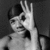 Black-and-white image of a person with short dark hair making an 'OK' hand gesture near their face, displayed in a four