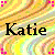 Pixelated static image with 'Katie' text over a multicolored abstract background featuring yellow, orange, green, and brown tones.