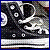 Pixelated static image of a dark figure with white circular eyes and limbs against a muted background, bordered by blue.