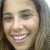 A person with long brown hair smiling broadly, showing white teeth, in a of three with varying facial expressions