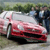 Pixelated image of a red and white car with a person standing behind it, set against a blurred green and gray background.