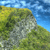 Pixelated landscape showing a rocky outcrop with green vegetation under a blue sky with scattered clouds.