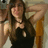 A pixelated image of a person with long dark hair wearing a black sleeveless top, holding an object near their head.