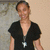 A person wearing a black V-neck top with a silver pendant necklace, standing against a light-colored wall with a blurred background.