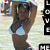 A woman in a light blue bikini top and dark bottoms poses with arms raised behind her head, set against a blurred outdoor background.