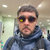 Pixelated image of a person wearing dark sunglasses with yellow reflection, blue jacket, and short dark hair against blurred background.