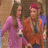 Two women in pink and orange outfits stand side-by-side; one woman's arm moves from her side to embrace the other.
