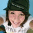 A person wearing a dark green cap and white shirt with text, smiling against a light blue background with a pink graphic element on the right.
