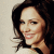 Pixelated close-up of a person with dark hair and light skin smiling, wearing a white top against a neutral background.