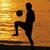 Silhouette of a person kicking a ball against a golden sunset background with horizontal light streaks.