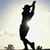 Pixelated black silhouette of a person swinging a golf club against a light gradient background with faint ground elements at the bottom.