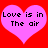 Two pink hearts on a red background with black text reading "Love is in The air" inside each heart.