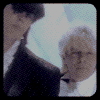 Animated sequence of two people in formal attire with changing facial expressions against a light background.
