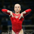 Static image of a gymnast in red leotard with arms extended horizontally against dark background, pixelated but recognizable as sports figure.