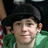 A person wearing a black cap and green hoodie with red-and-white checkered background, shown in three