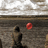 Pixelated static image shows a dark silhouette figure against textured background with red circular object on right.