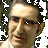 Pixelated close-up of a person's face with light skin tone, dark hair, and glasses, set against a blurred green and gray background.