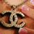 A pixelated close-up of a metallic anchor pendant with interlocking rings, set against warm-toned blurred background.