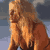 Pixelated static image of a person with long light brown hair wearing an orange bikini top against a blue-gray background.