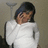 Pixelated image of a person with dark hair wearing a white shirt against a neutral background with a lamp visible.