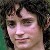 Pixelated close-up of a person with dark curly hair and light skin, cropped to show the head and upper shoulders against a dark background with green and brown tones.