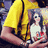 A pixelated image shows a person in yellow clothing holding another figure with long dark hair and white top, set against a blurred background.