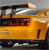 Yellow vehicle with dark roof and red interior visible through side window, positioned on dark ground with light background.
