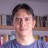 Pixelated static image of a person with dark hair wearing a blue shirt against a blurred background with indistinct shapes and colors.