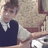A pixelated image shows a person in a dark vest over light shirt seated at a table with patterned fabric background, below black section with partial white text.