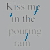 Gray background with repeated text 'Kiss me in the pouring rain' and scattered blue pixel fragments resembling water droplets.