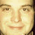 Pixelated close-up of a person's face showing eyes, nose, mouth, and partial hair with warm-toned skin and light background.