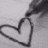 Black-and-white pixelated image showing a hand drawing a heart shape on textured paper with text reading 'Dylan Jenni 9.24.07' in blocky font.