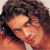 Pixelated close-up of a person with dark curly hair and light skin, wearing a white shirt against an orange background.